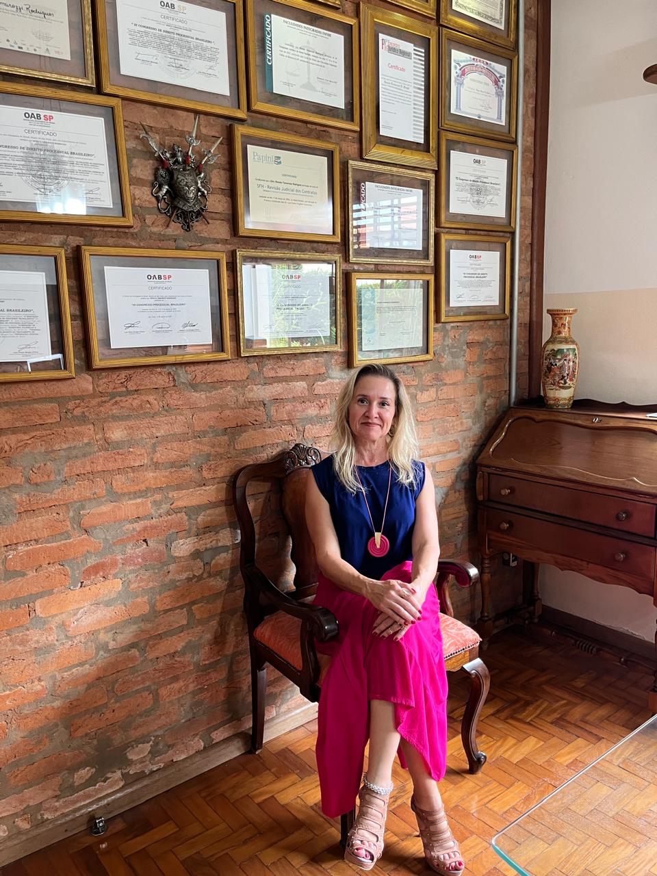 Dra. Renata Tamarozzi Rodrigues em seu escritório com diplomas e certificados